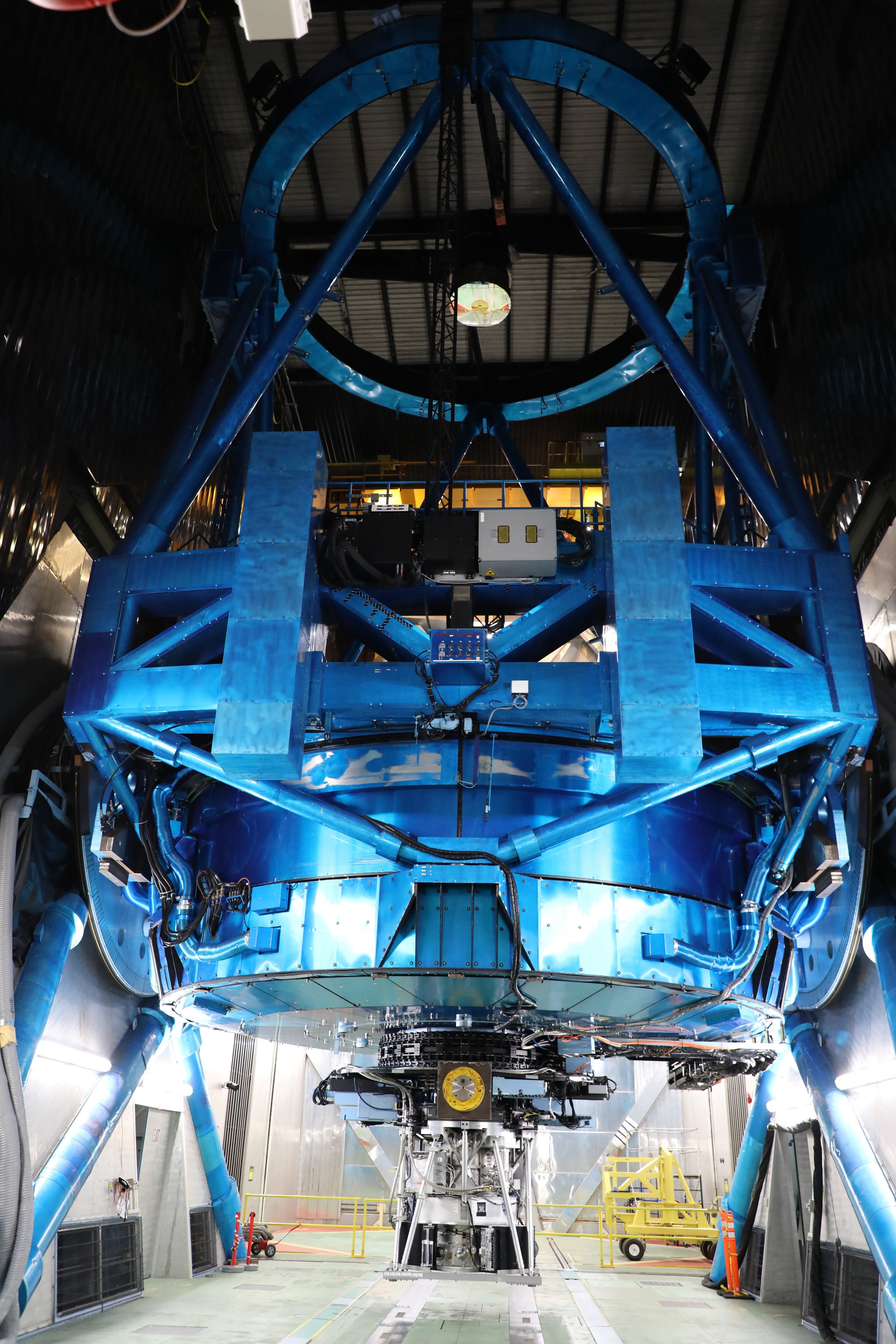 Interior of a large scientific or industrial machine with blue structural components, wiring, and a central circular ring at the top in a high-ceiling room.