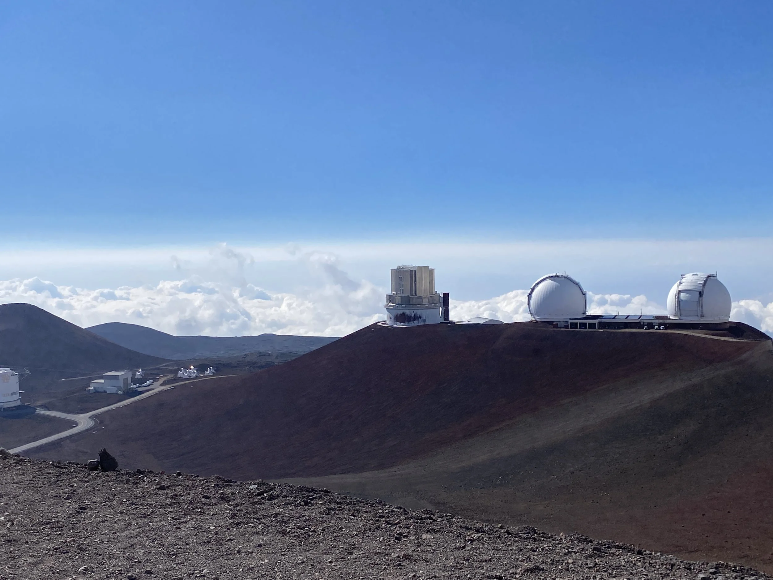 View of a mountain landscape with observatory telescopes on the summit, under a clear blue sky with scattered clouds.