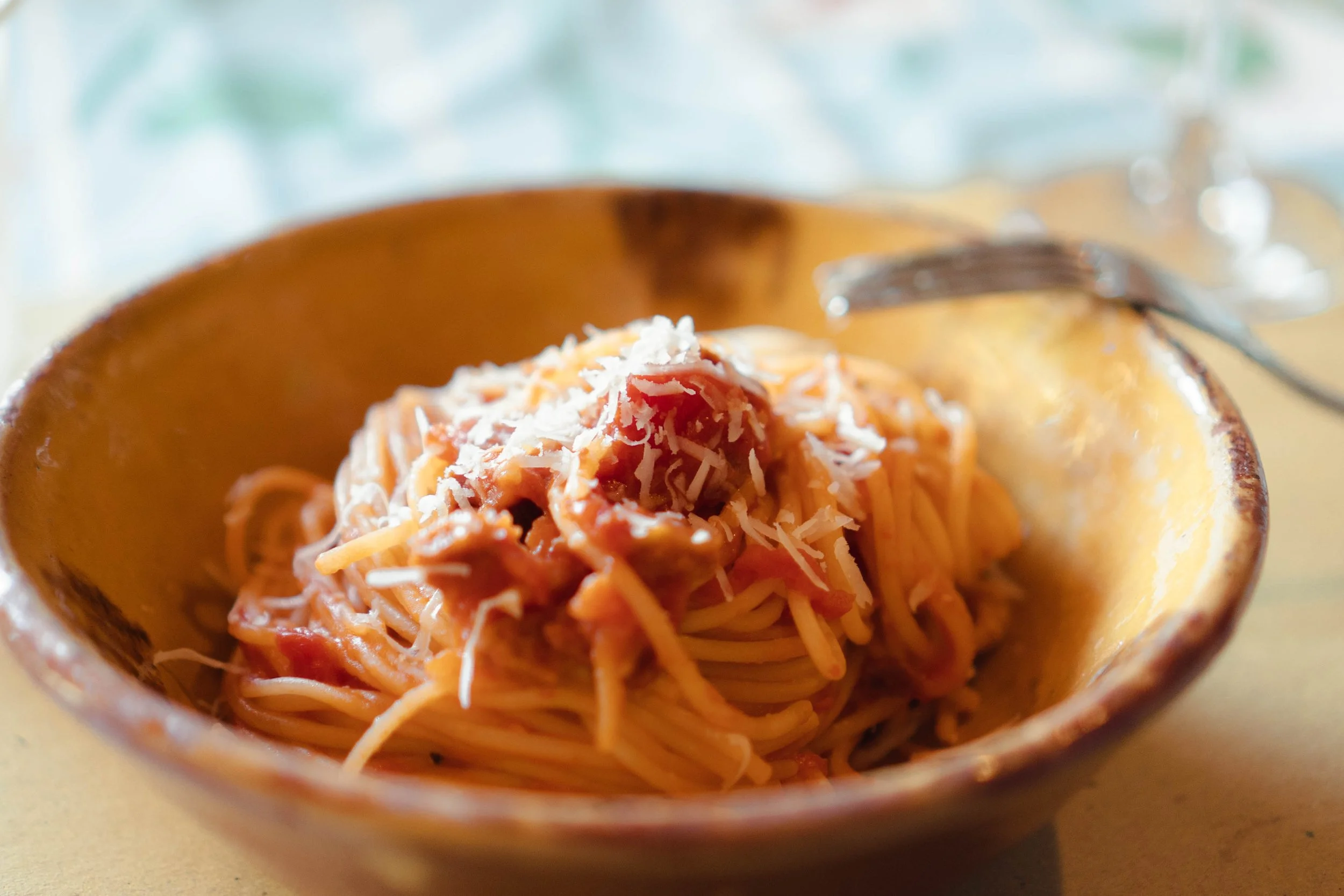 A bowl of spaghetti with tomato sauce and shredded cheese on top.