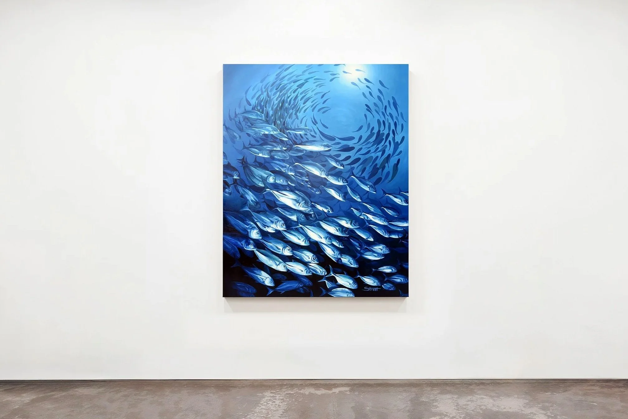 Painting of a school of fish swimming in the ocean with sunlight overhead, displayed on a white gallery wall.