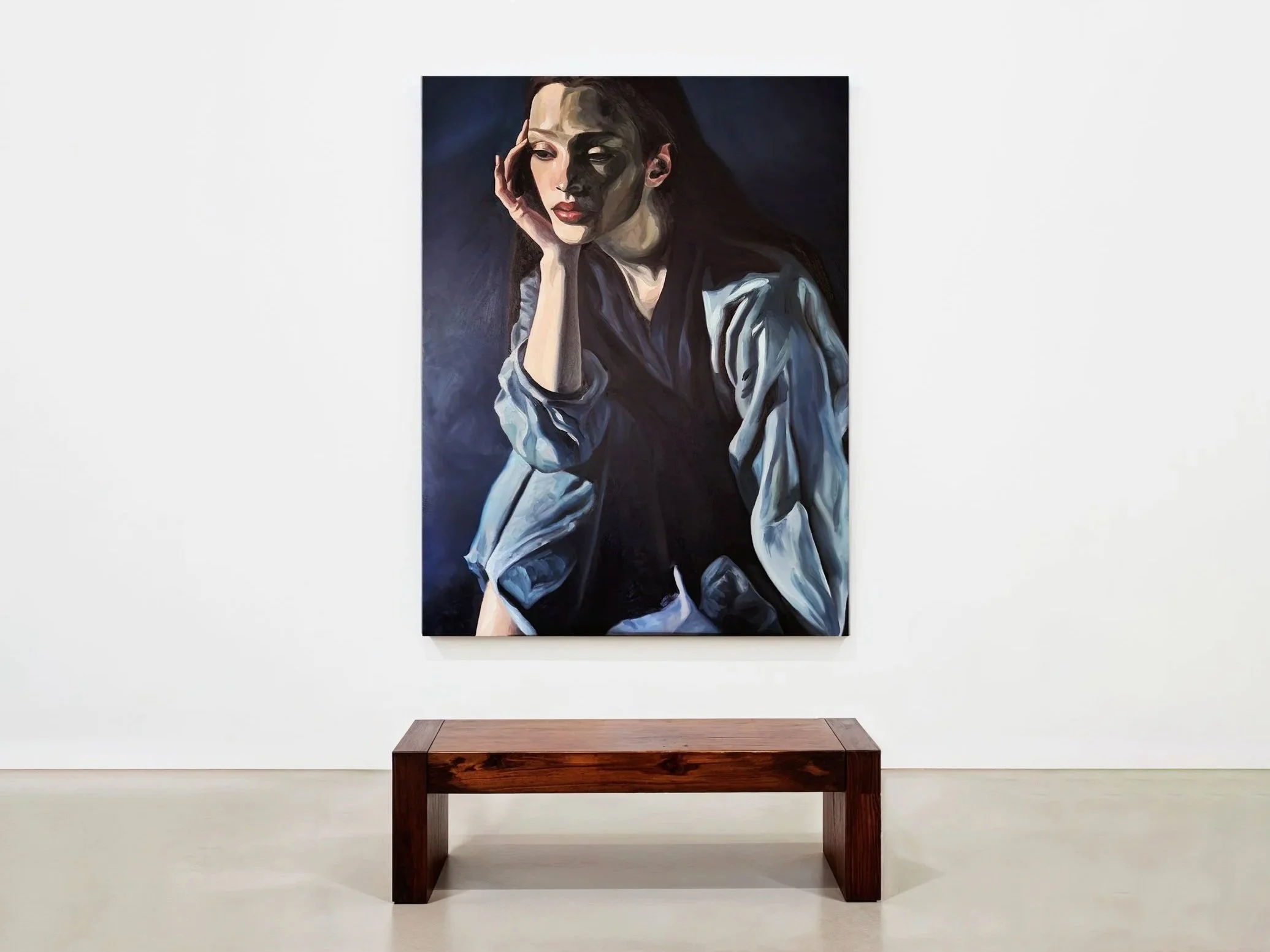 Painting of a woman with long dark hair, resting her head on her hand, wearing a striped shirt and a dark scarf, displayed on a white gallery wall.