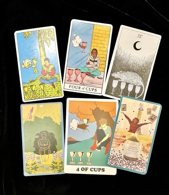 Six Four of Cups cards by indie tarot artists are displayed on a black surface in two neat rows.