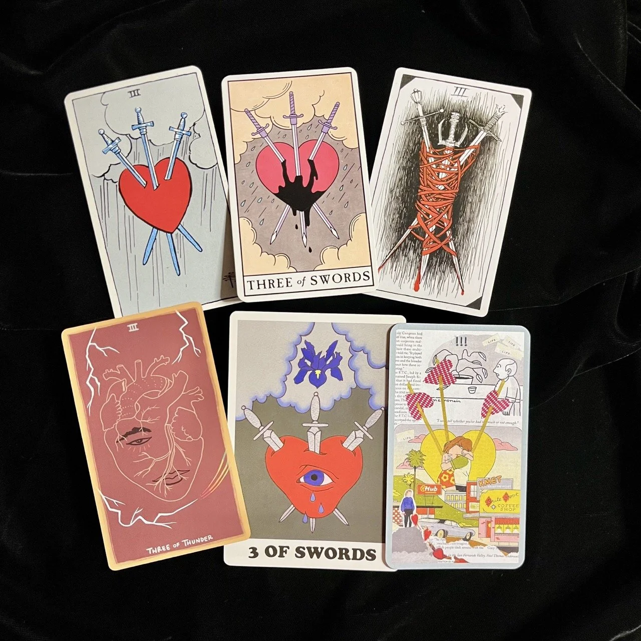 Six examples of the Three of Swords tarot cards arranged on a black cloth.