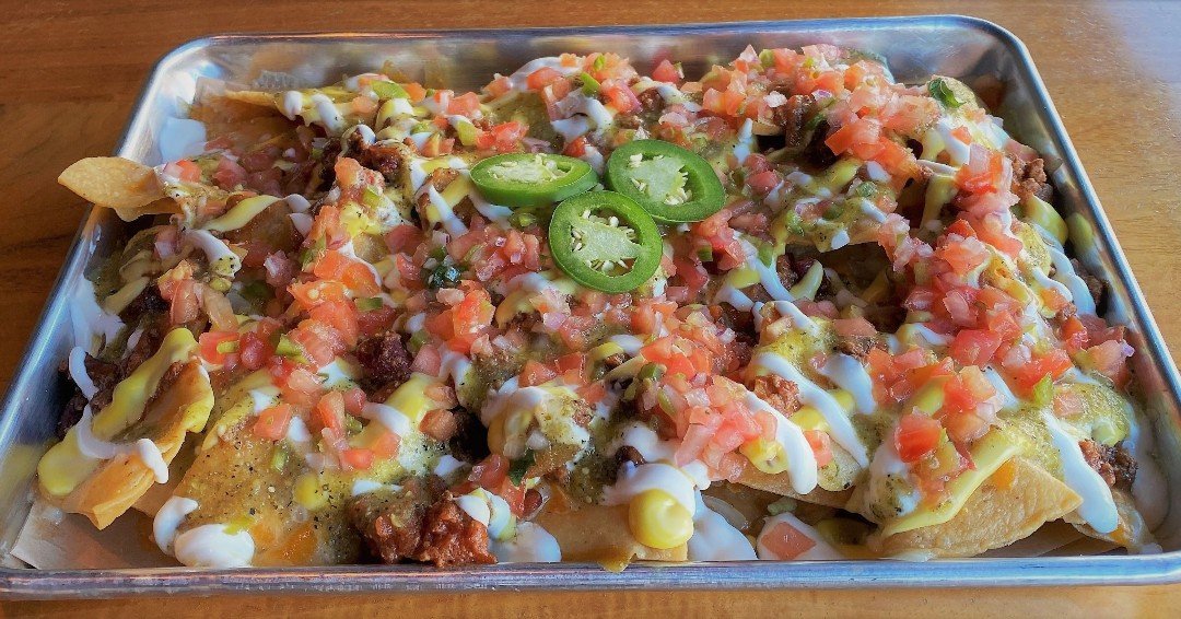 Our Nachos are loaded! Tortilla chips topped with our Seven-Pepper Chili (custom beef blend, seven peppers, onions, kidney beans), shredded cheddar, cheddar cheese sauce and sour cream + house salsa verde and pico de gallo. It's National Nachos Day -