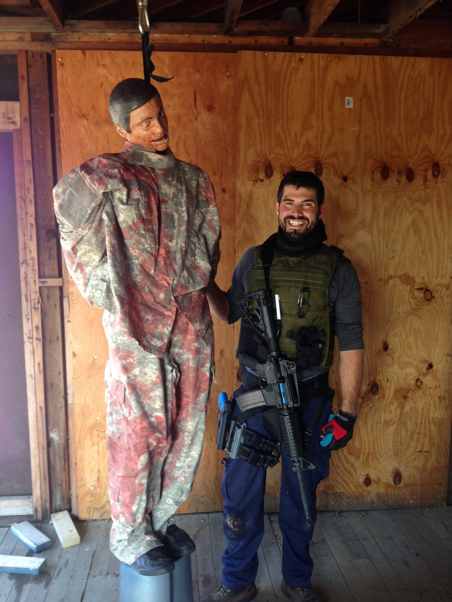 Smiling man acting as a Terrorist and posing with hanging human dummy in preparation for high threat environment training
