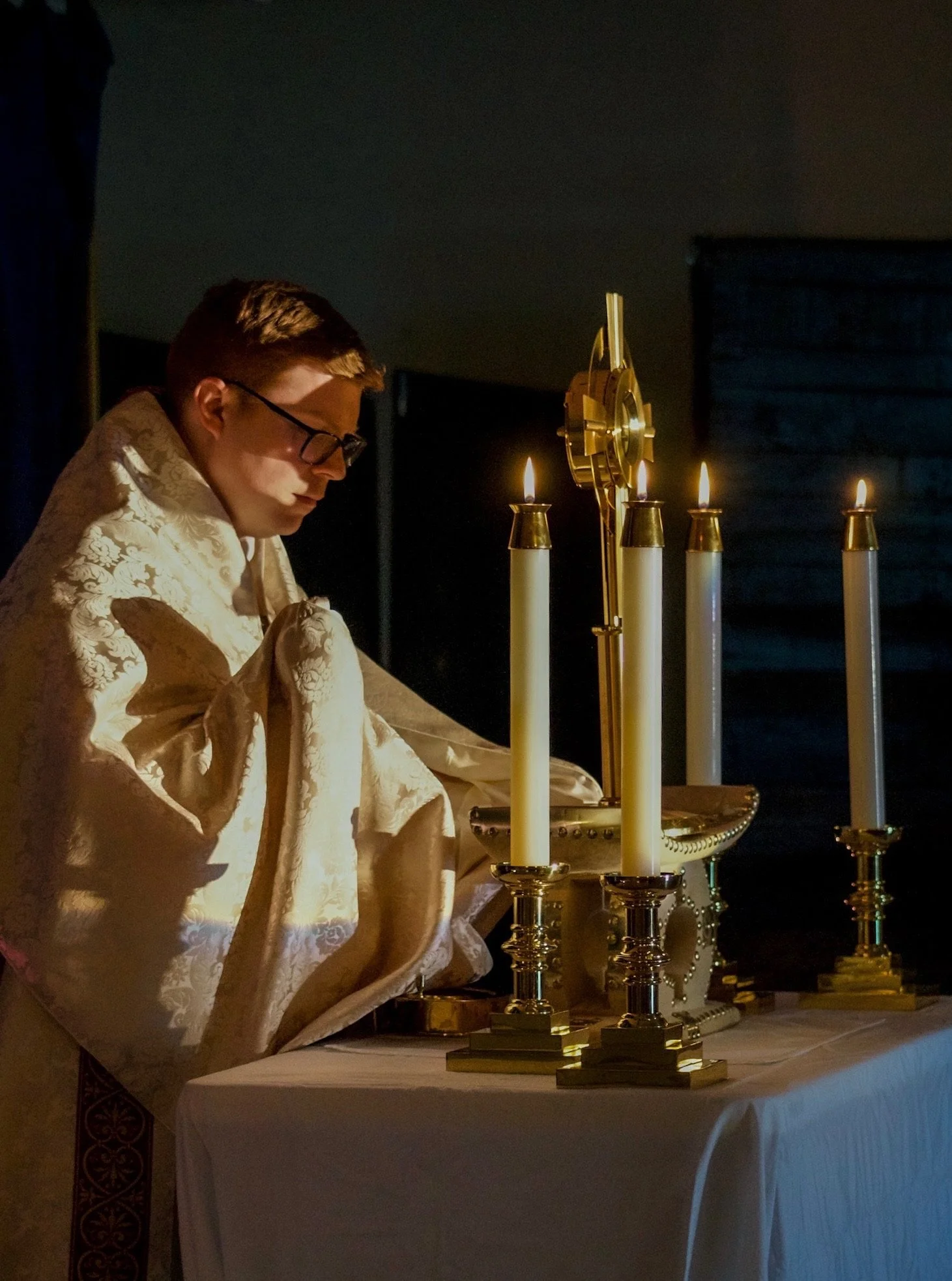 A golden monstrance with decorative rays and small jewels on a white table against a plain wall.
