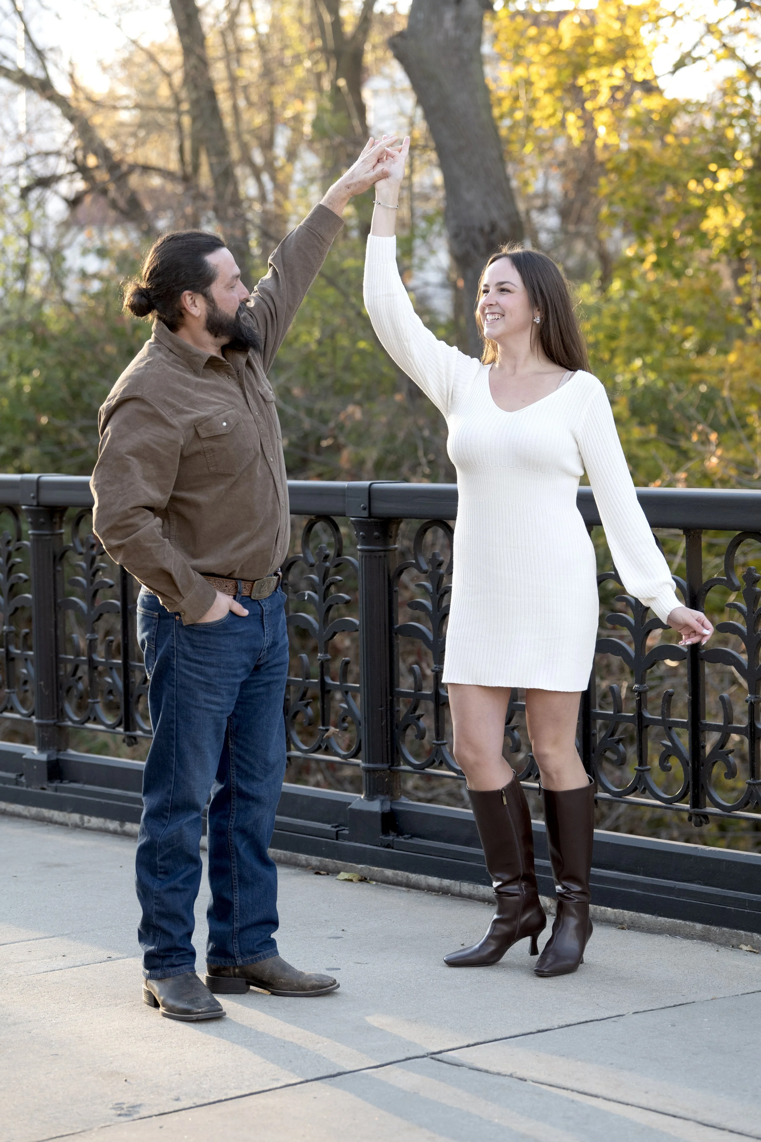 A man and woman dancing together outdoors on a bridge, with autumn leaves in the background.