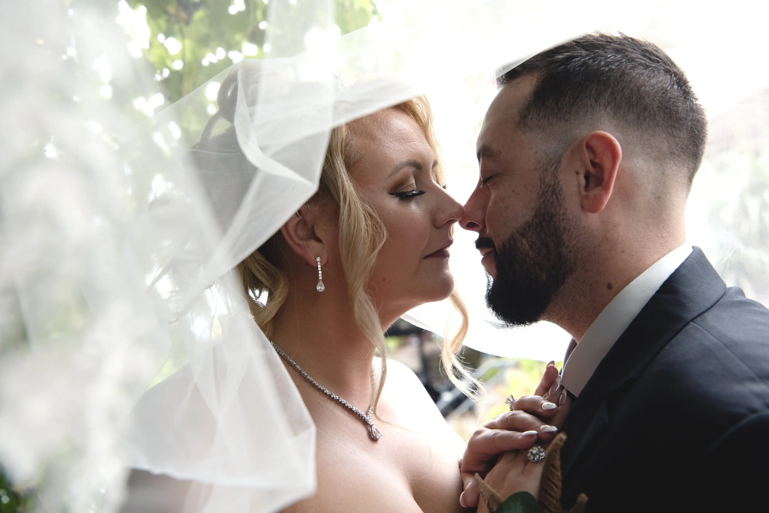 A bride and groom face each other closely, touching foreheads during their wedding ceremony, with a veil softly obscuring part of the scene.
