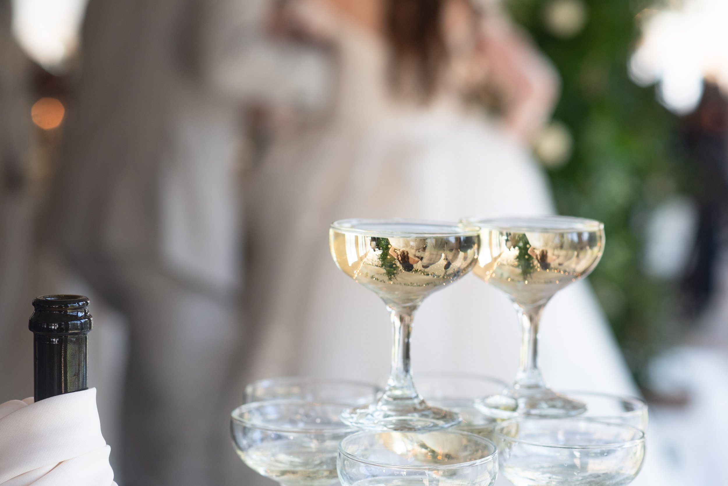 Close-up of four champagne glasses filled with champagne, with a blurred background of a person and Christmas decorations.