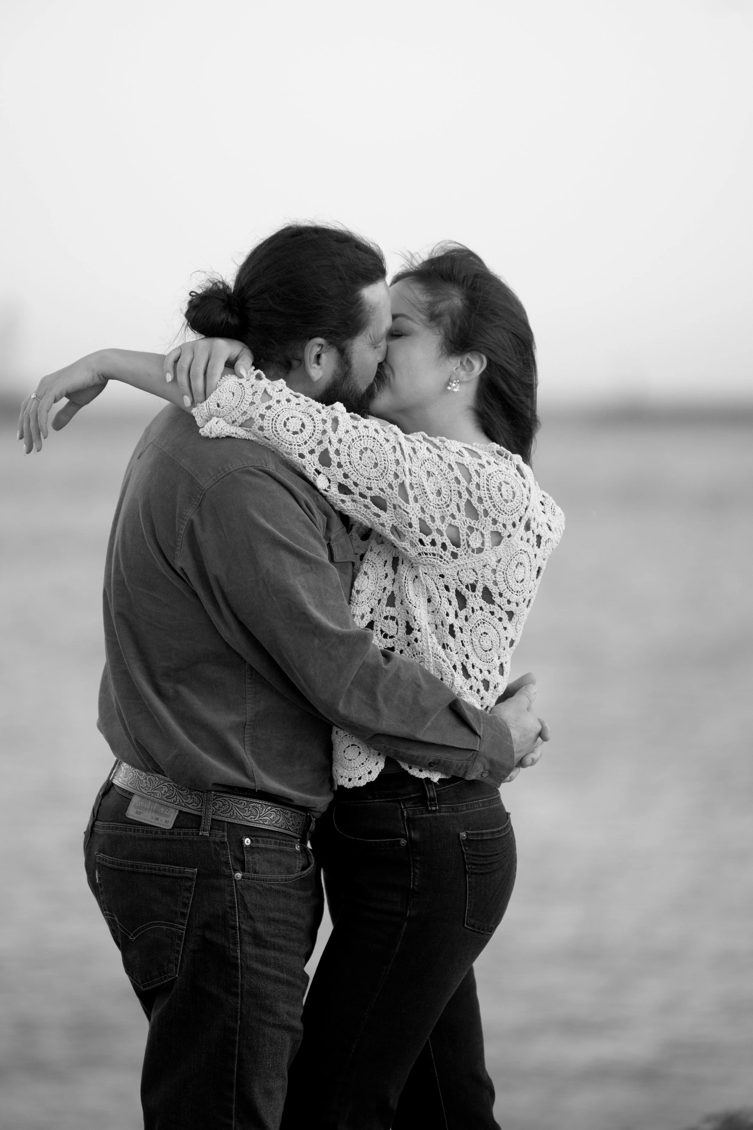 A couple embracing and kissing on a beach in black and white.