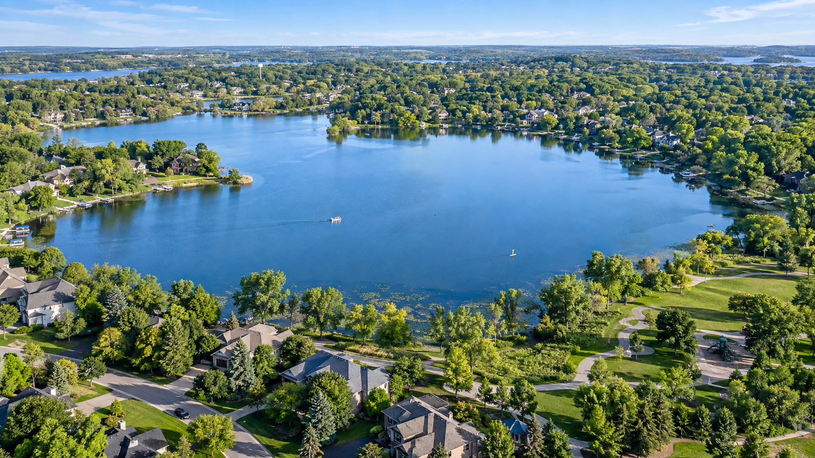 Aerial view of a neighborhood around a large lake with houses, trees, boat, and lush greenery.