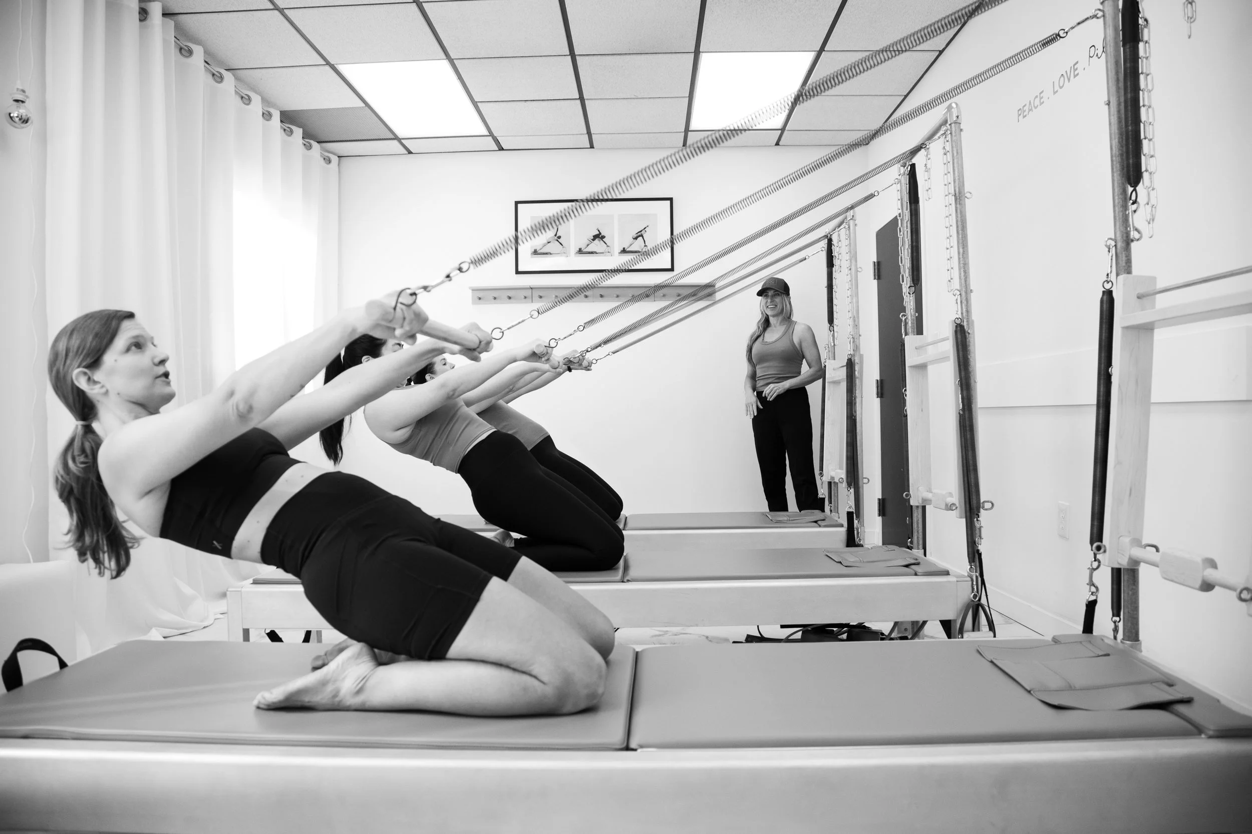 Women participating in a Pilates class on reformer machines, supervised by an instructor in a fitness studio.