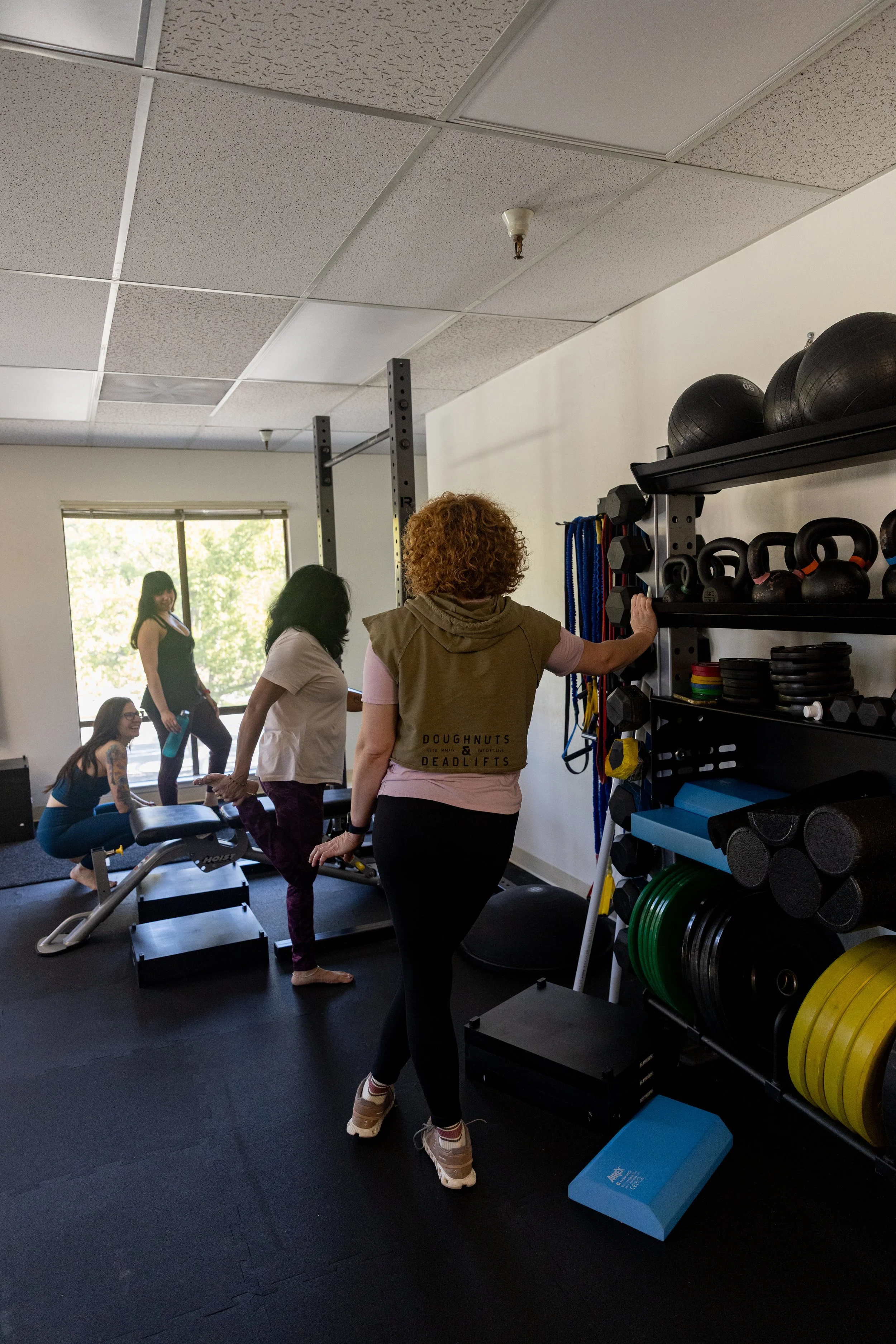 Four women in workout clothes celebrating with high fives in a gym with exercise equipment in the background.