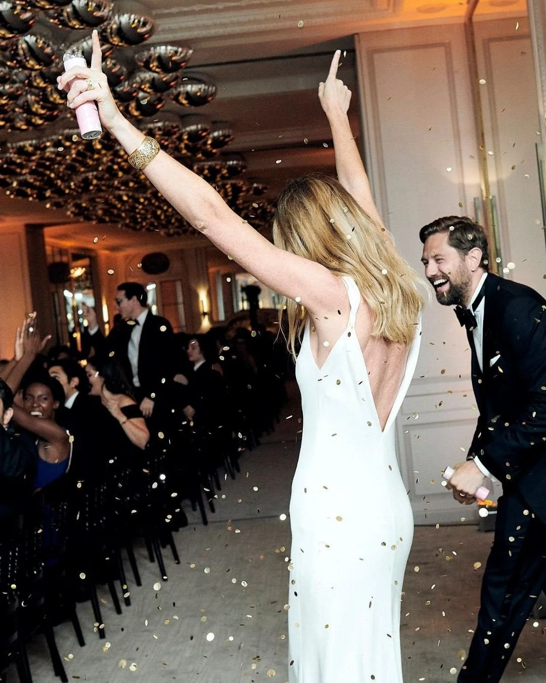 The kind of entrance that changes the rhythm of the room. Doors open, music builds, the couple walks in with intention. Laughter, cheers, a skyline glowing beyond the glass. The setting is classic Paris, but the mood is modern. Structured silhouettes