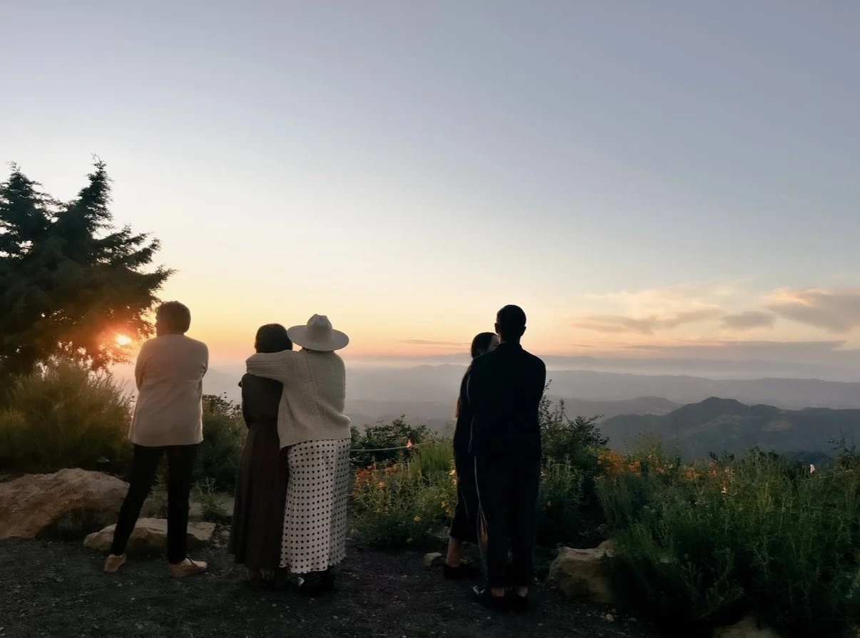 Group of people watching a sunset over layered mountain ranges from a scenic overlook