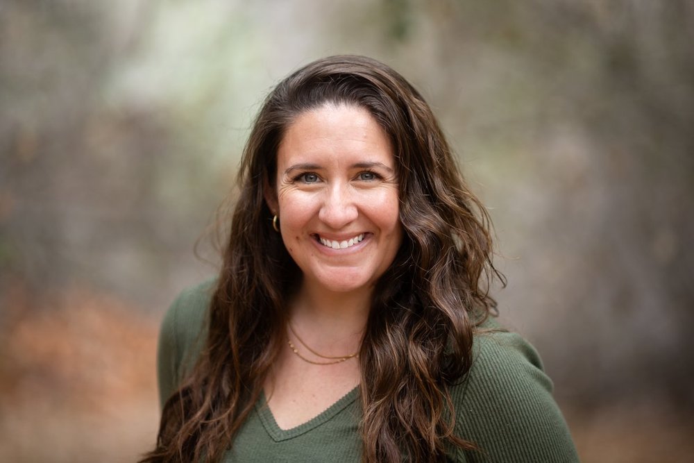 Professional outdoor headshot with a softly blurred natural background