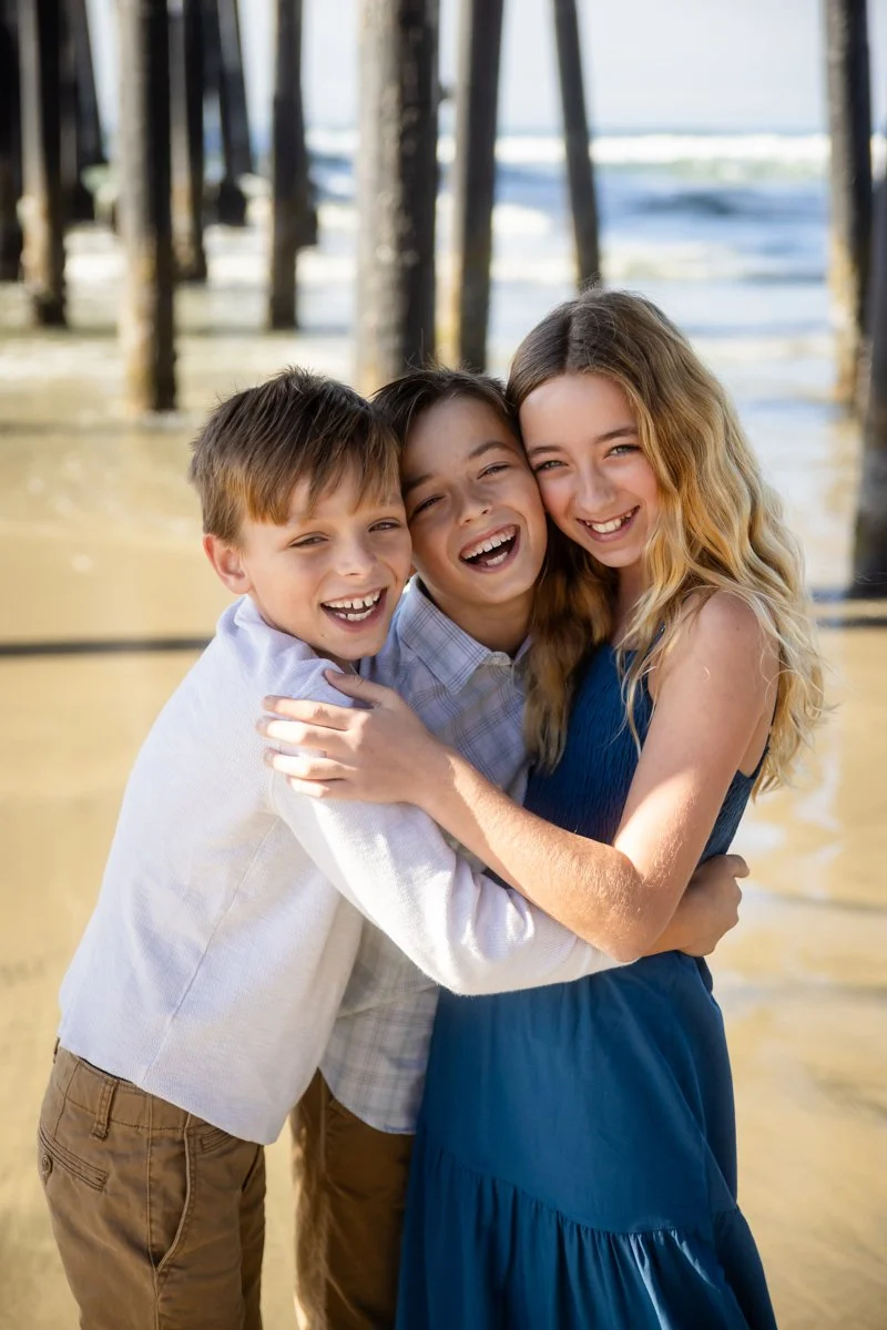 Three siblings embracing on the beach during a children&rsquo;s portrait session
