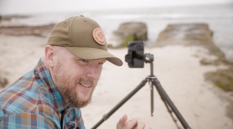 Joseph on the beach with a camera on a low tripod, explaining framing