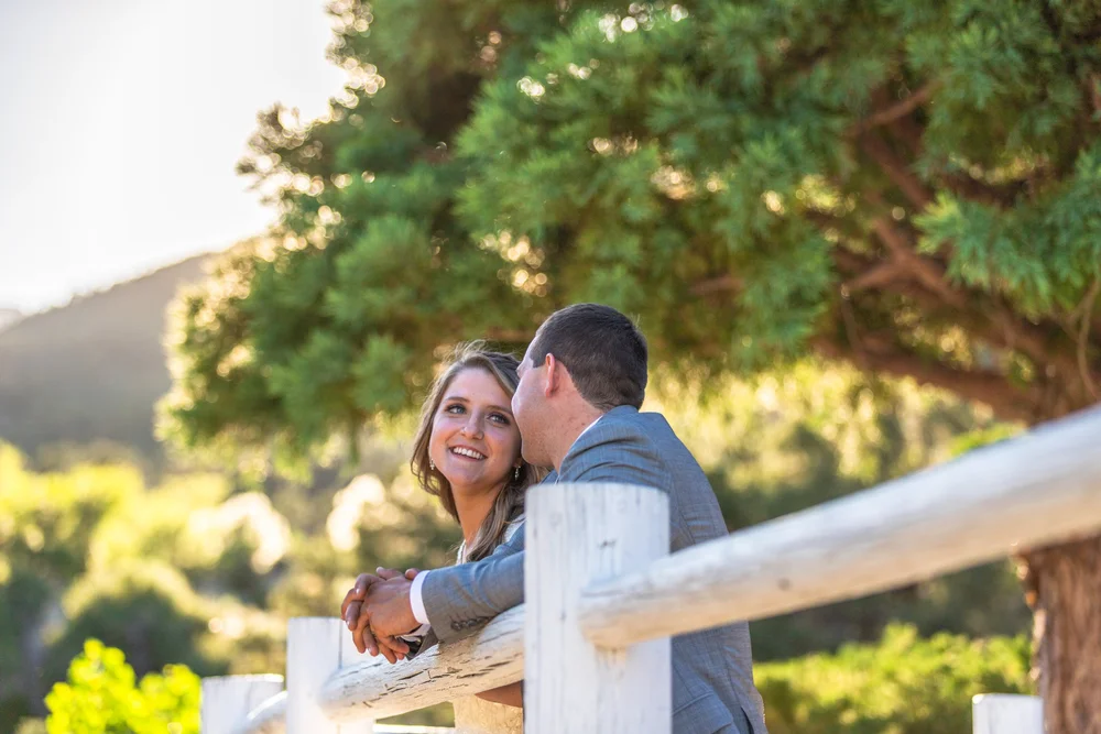 Bride and groom embracing on a wooden deck railing with pine trees and a mountain view behind them on Mount Charleston