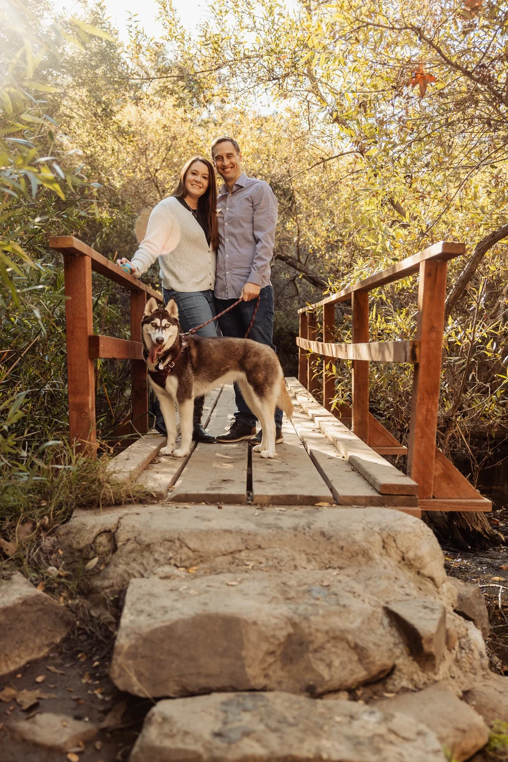 Couple posing with their husky on a stone footbridge along the canyon trail in Rancho Penasquitos
