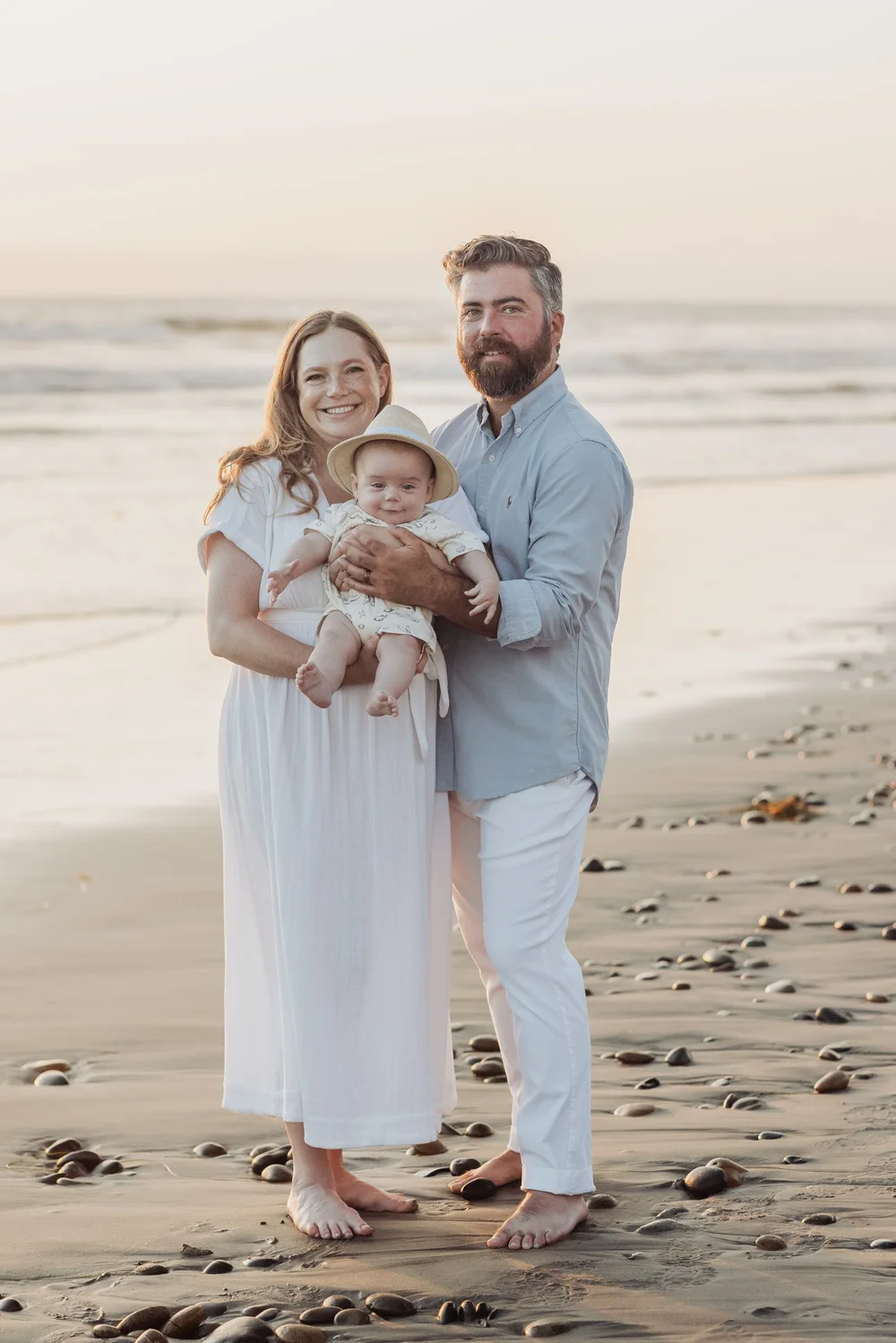 Parents holding their swaddled newborn on the beach in Carlsbad, San Diego