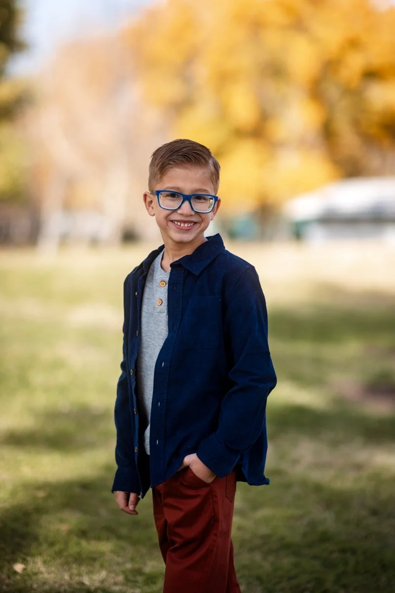 Smiling boy with glasses standing in a grassy field during a portrait session