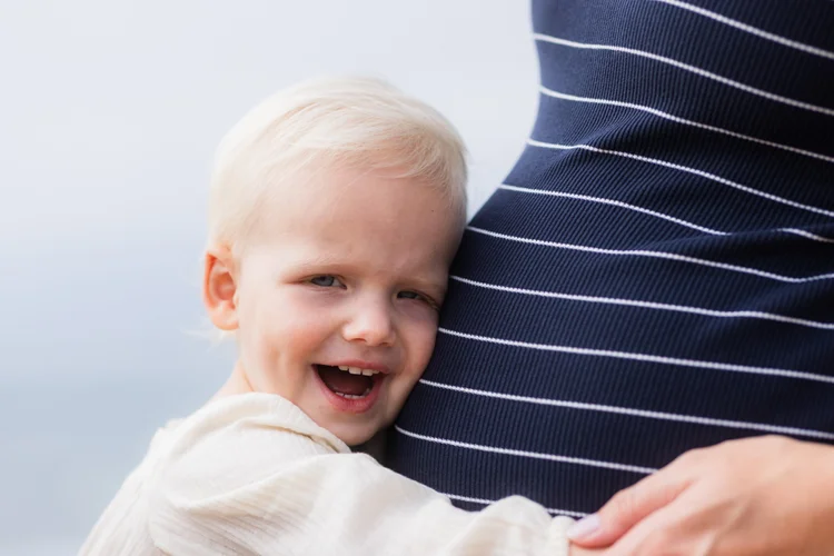 Toddler laughing against a parent’s bump during a maternity session in Carlsbad