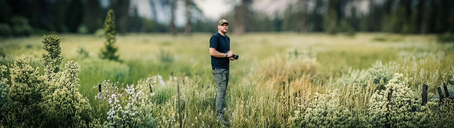 Joseph standing in a mountain meadow with a camera