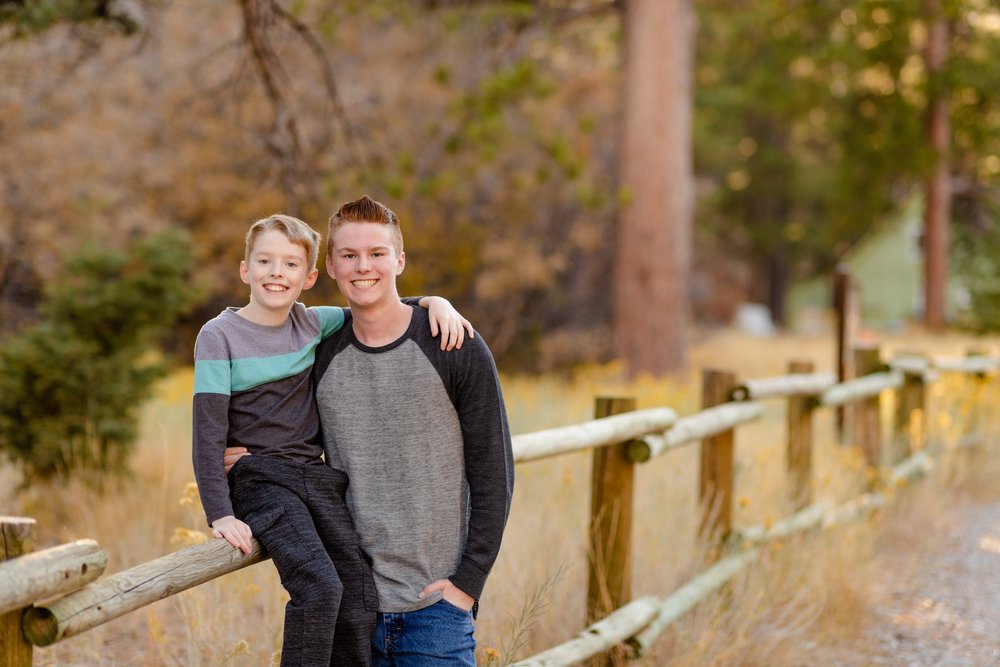 Father and young son leaning together on a wooden split-rail fence with a forest backdrop on Mount Charleston