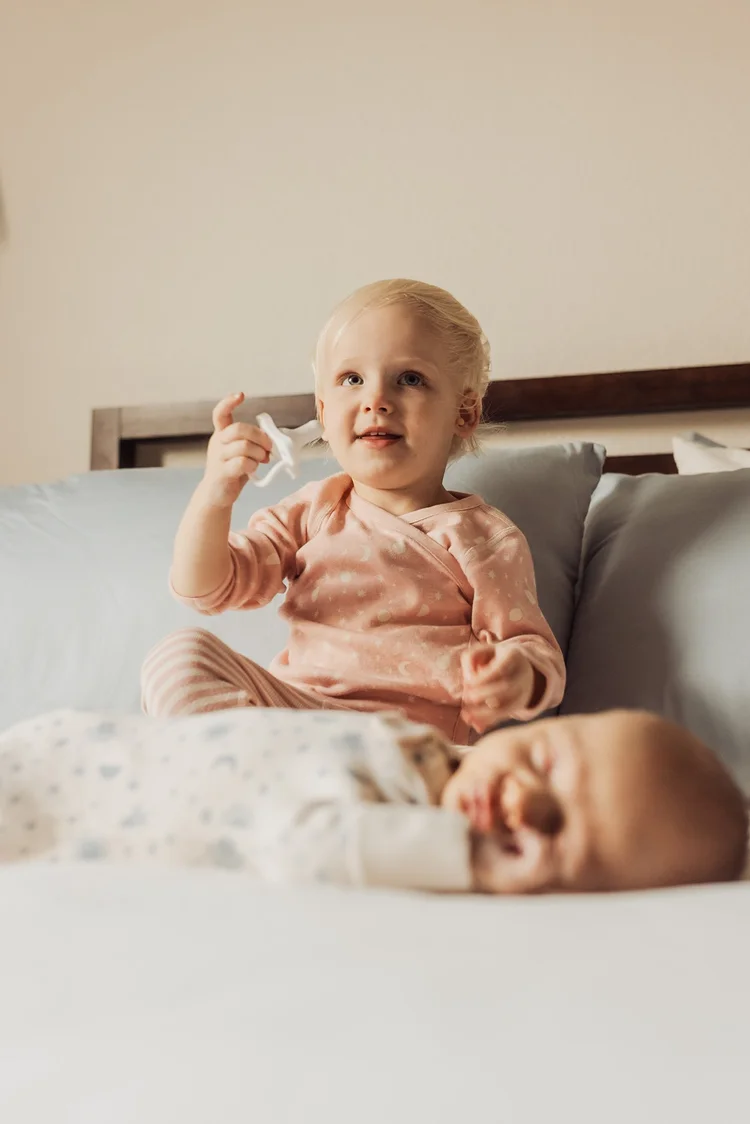 Older sibling sitting beside a newborn on a bed at home