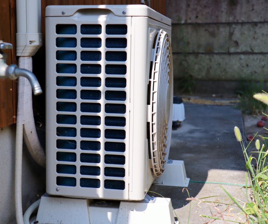 Outdoor air conditioning unit on a concrete pad next to a wooden wall.