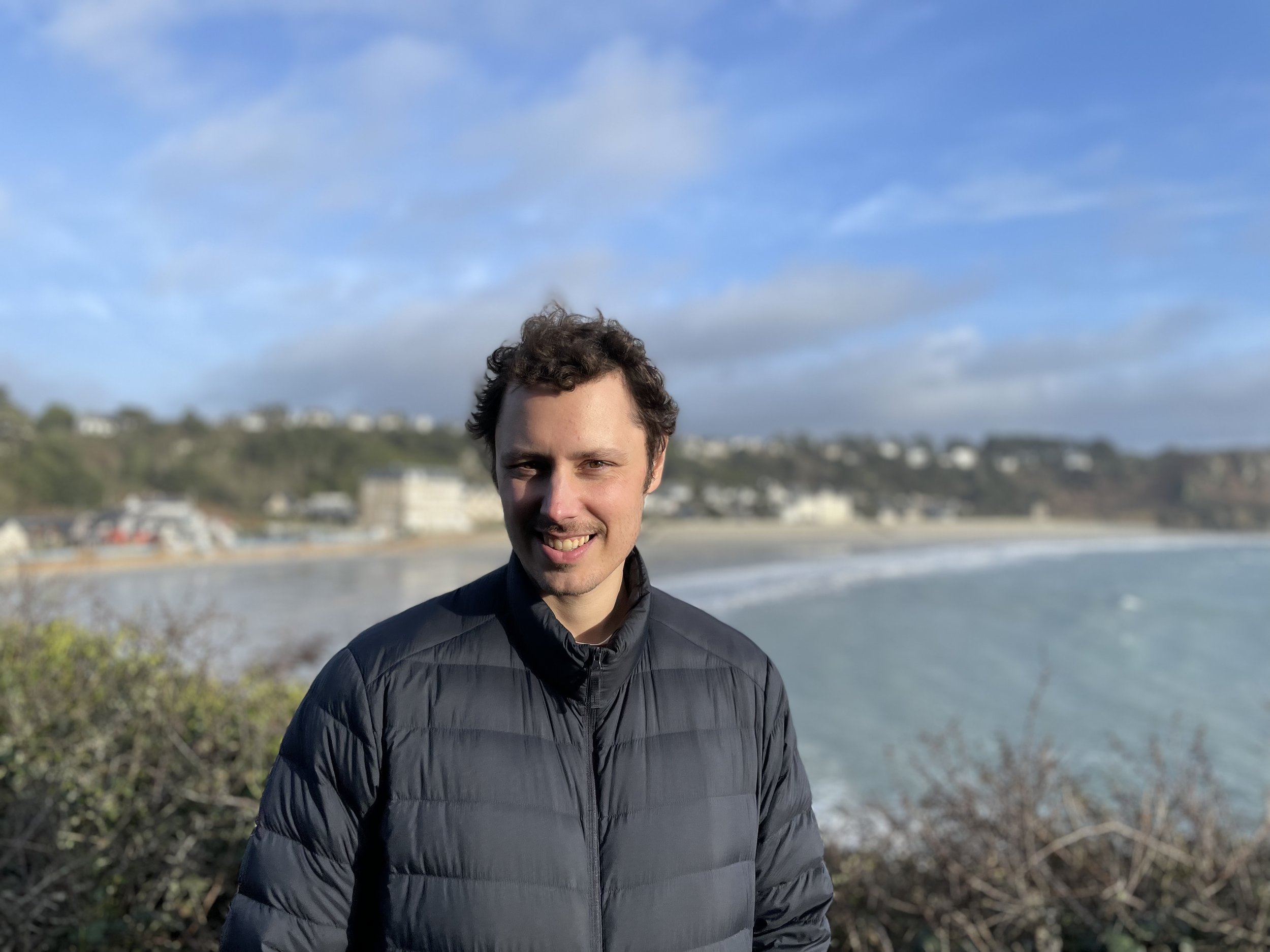 Man smiling with a bush, water and beach in the backgroundnd