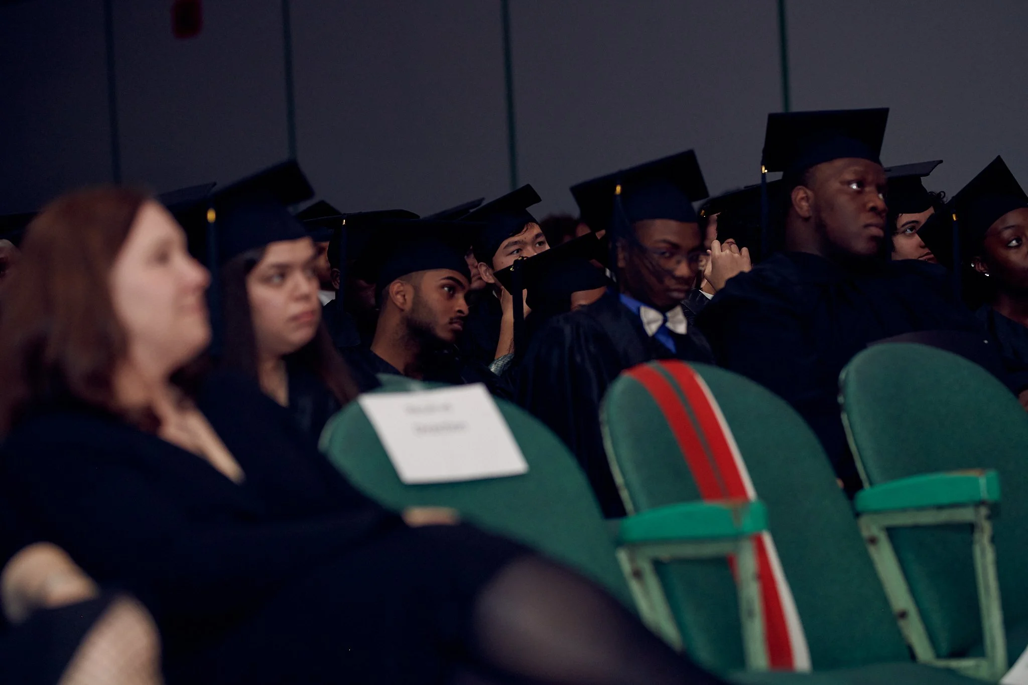 Étudiants en graduation portant des toques et robes noires assis dans une salle.