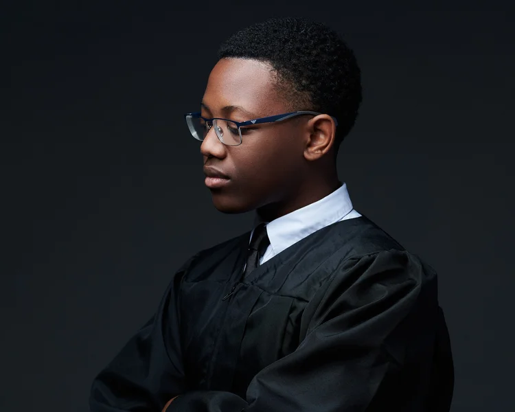 Portrait d'une personne de profil portant des lunettes et une veste noire, contre un fond sombre.