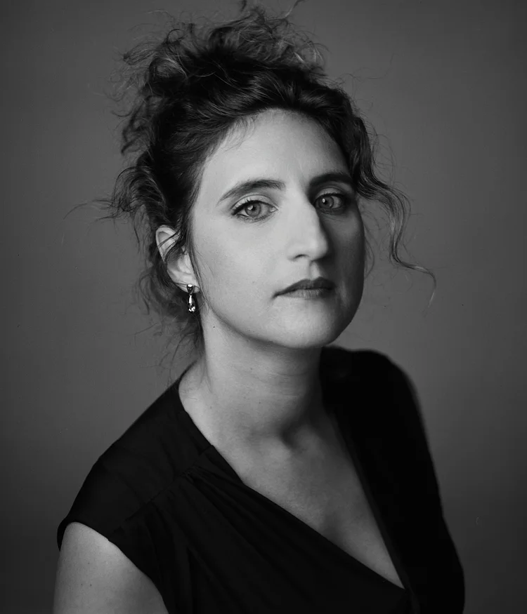 Portrait en noir et blanc d'une femme avec des cheveux bouclés coiffés en chignon, portant une robe noire et des boucles d'oreilles pendantes.