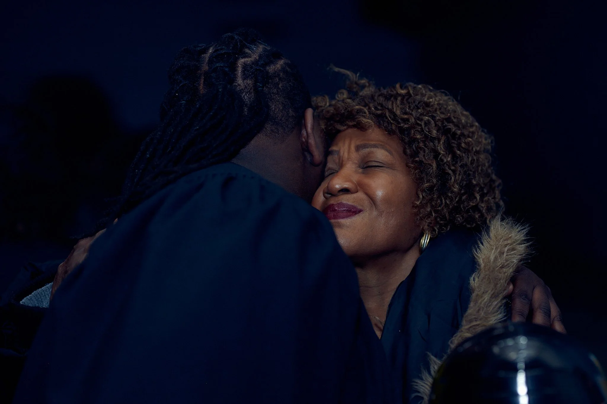 Deux personnes s'embrassent tendrement dans une scène émouvante, dans un environnement sombre.