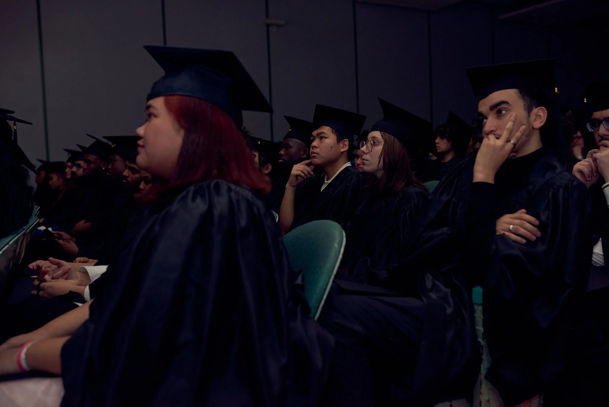Étudiants en robes de graduation et chapeaux assis dans une salle de cérémonie.