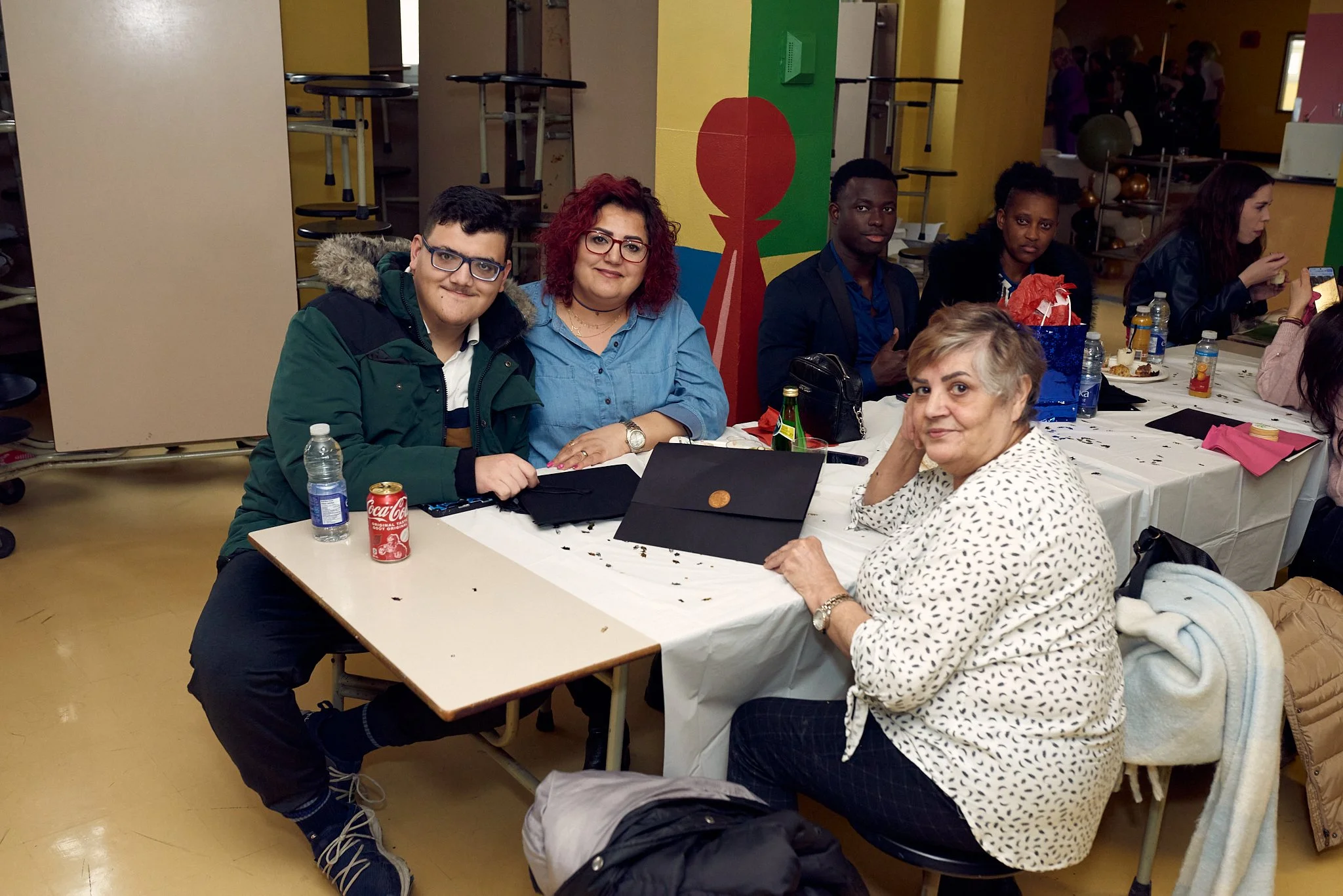 Groupe de personnes assises autour d'une table lors d'une fête ou d'un repas, décorée avec un fond coloré.