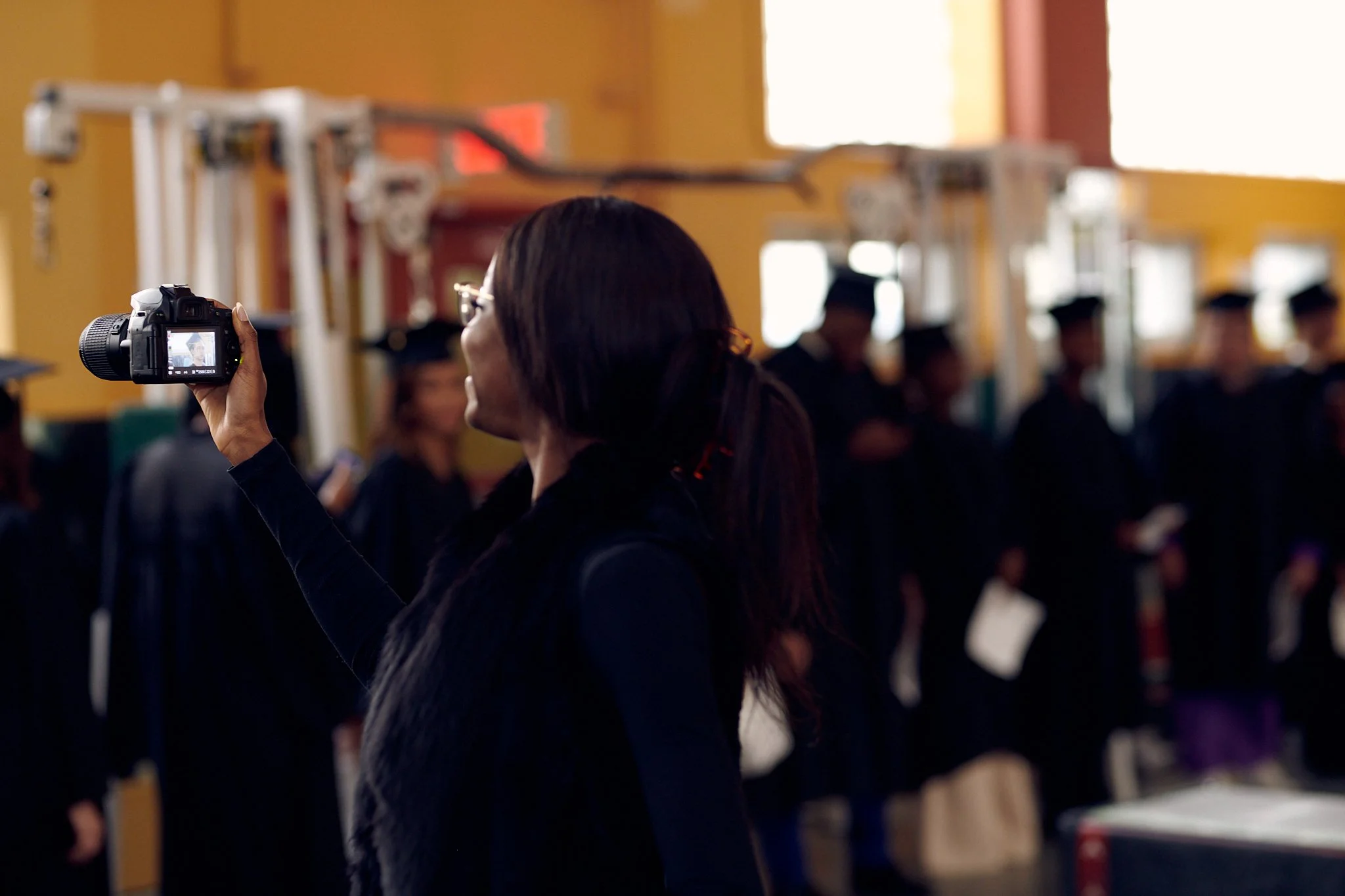Femme photographiant un groupe de diplômés lors d'une cérémonie de remise de diplômes en intérieur.