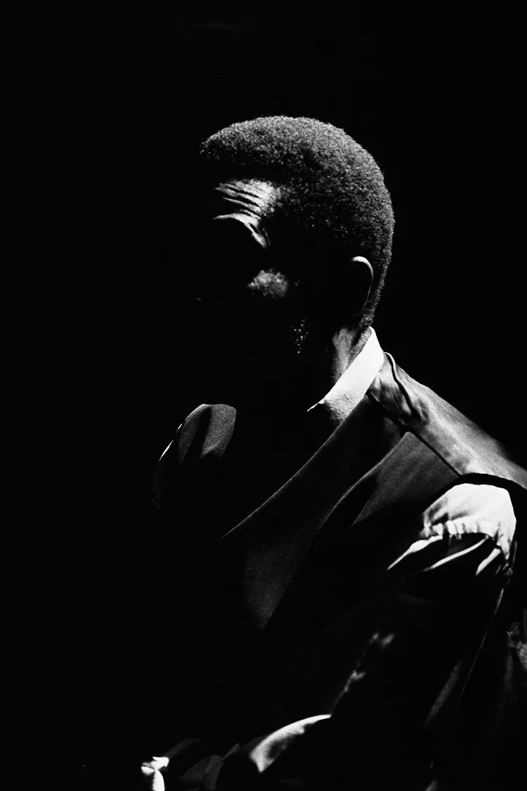 Portrait noir et blanc d'un homme avec un visage partiellement dans l'ombre, portant une chemise claire, avec un regard pensif.