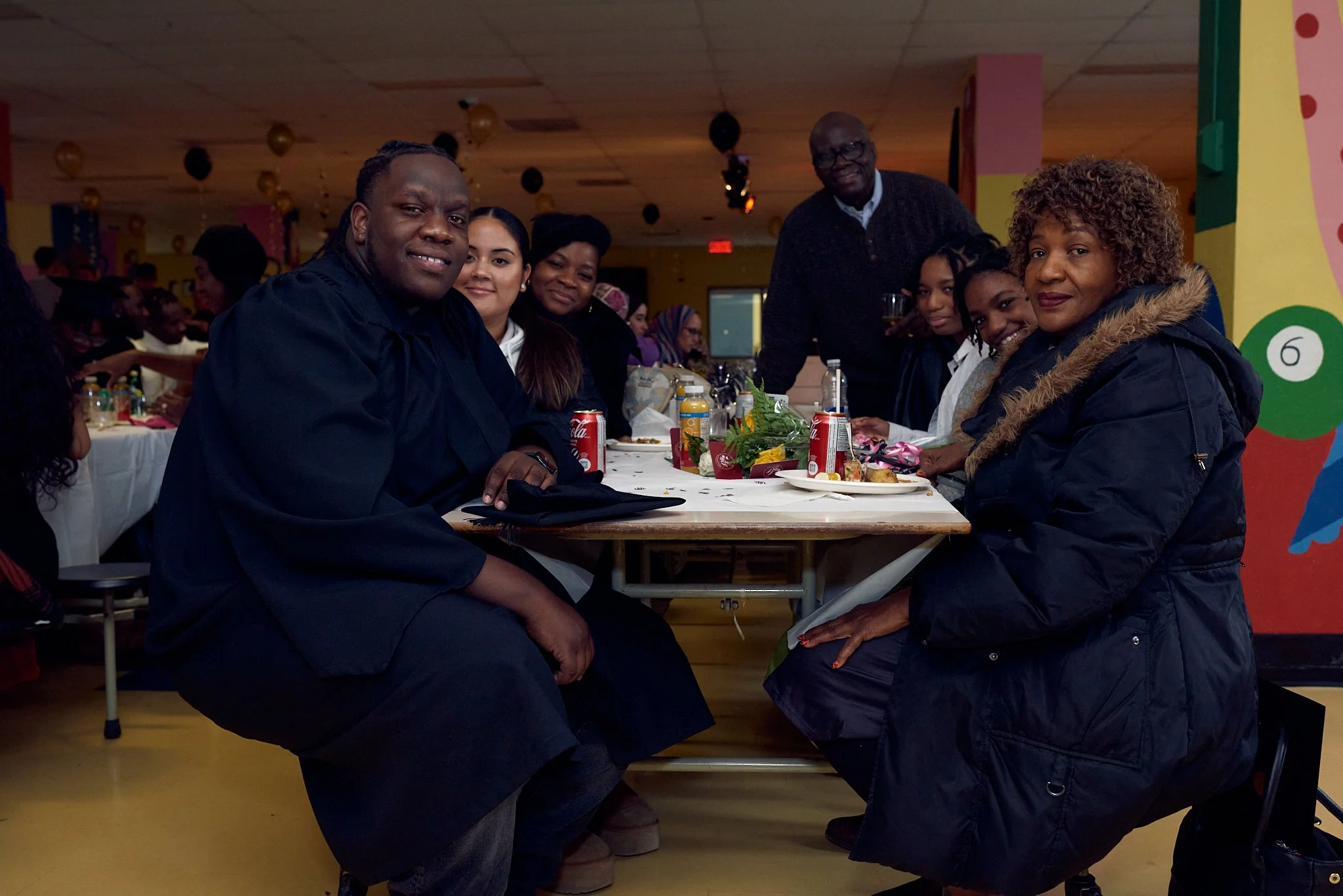 Un groupe de personnes assises autour d'une table lors d'un repas ou d'une célébration dans une salle colorée.