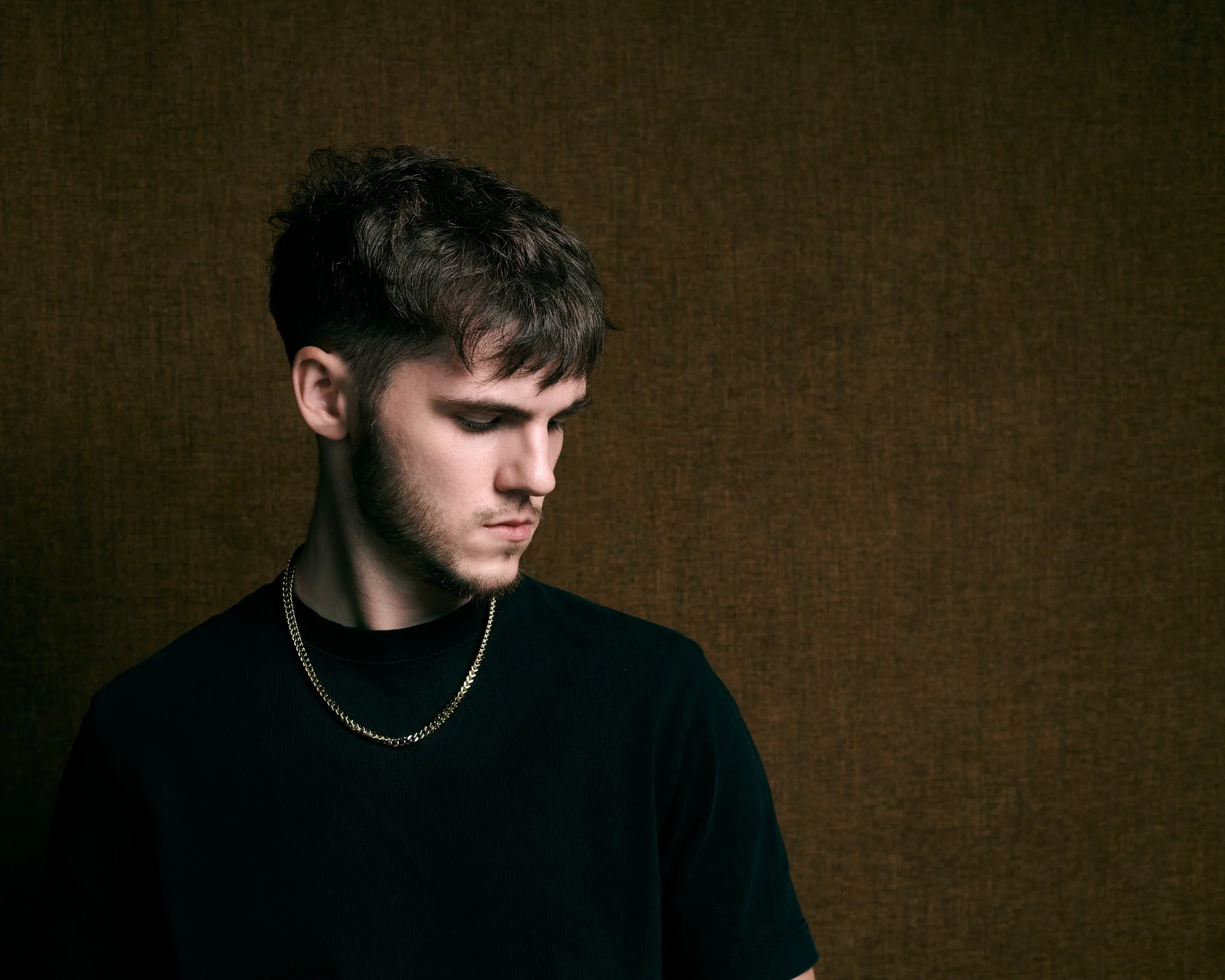 Jeune homme avec des cheveux courts, porter un chandail noir, un collier en chaîne et un fond marron