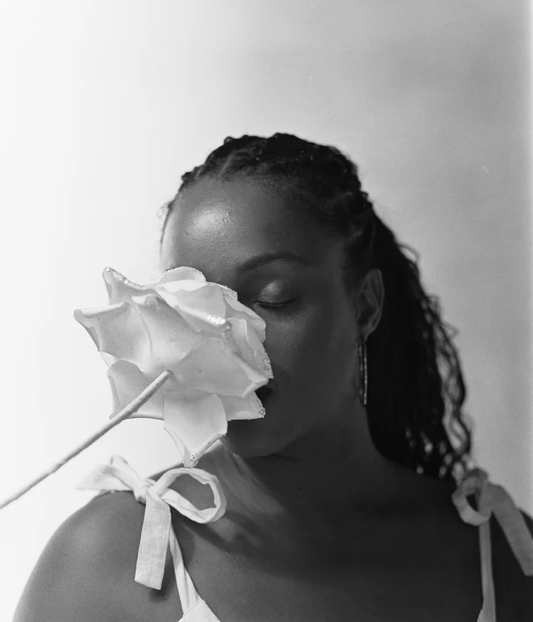 Une femme avec des cheveux bouclés couvre partiellement son visage avec une grande fleur blanche.