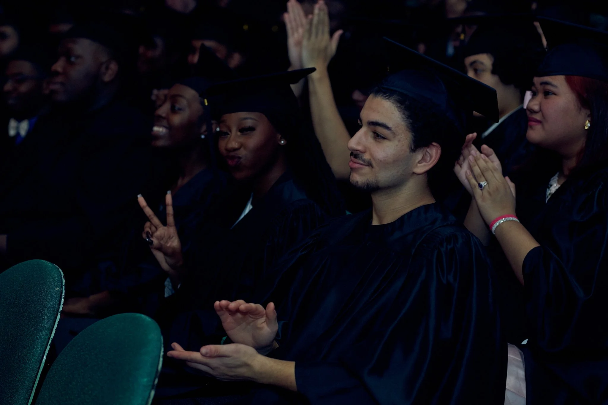 Groupe d'étudiants en toges de graduation, certains applaudissent, d'autres font des gestes de paix, lors d'une cérémonie de remise de diplôme.