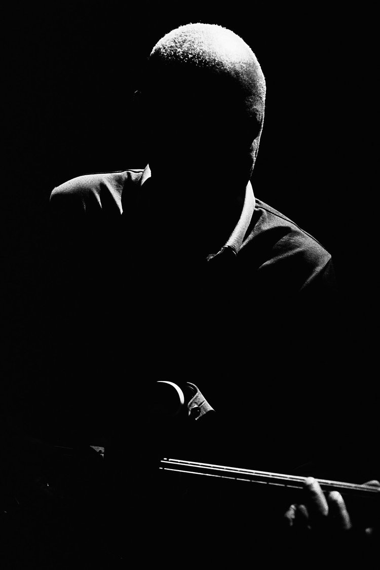 Une silhouette sombre d'une personne jouant du piano, éclairée partiellement par une lumière venant de la droite, avec un fond noir.