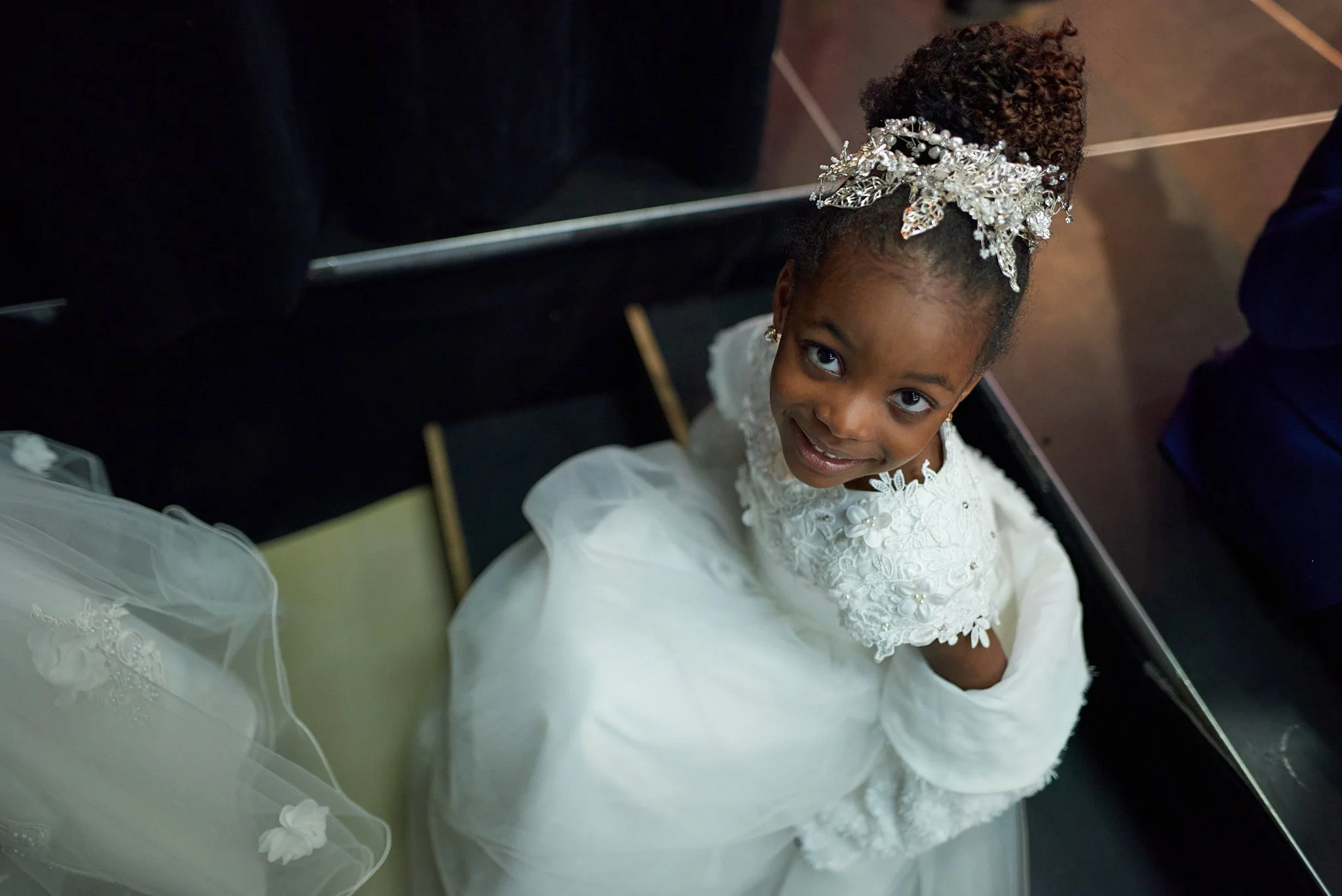 Jeune fille en robe de mariage blanche avec une couronne de fleurs, regardant vers le haut avec un sourire.