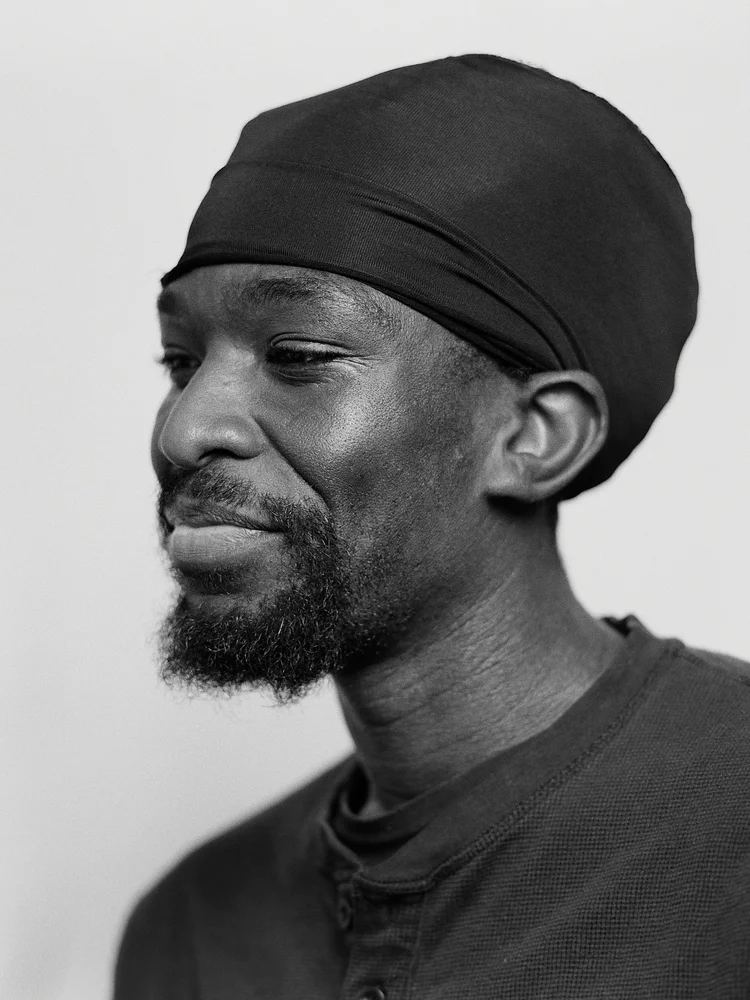 Portrait d'un homme portant un turban noir et un t-shirt gris, en photographie noir et blanc.