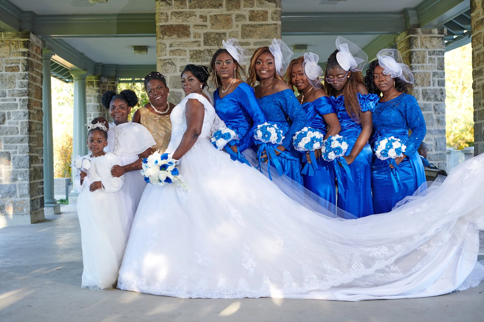 Groupe de femmes et deux jeunes filles en robe de mariage et de demoiselle d'honneur, posant en extérieur devant un mur en pierre, pour une photo de mariage.