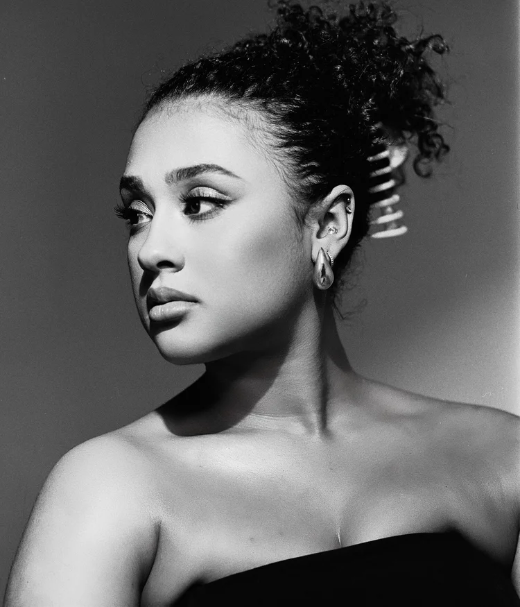 Portrait en noir et blanc d'une femme avec des boucles brunes, portant plusieurs boucles d'oreilles et un maquillage subtil