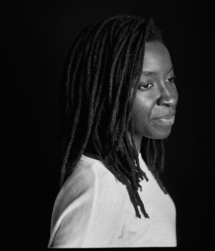 Portrait en noir et blanc d'une femme avec des dreadlocks, regardant vers le bas, portant un haut clair.